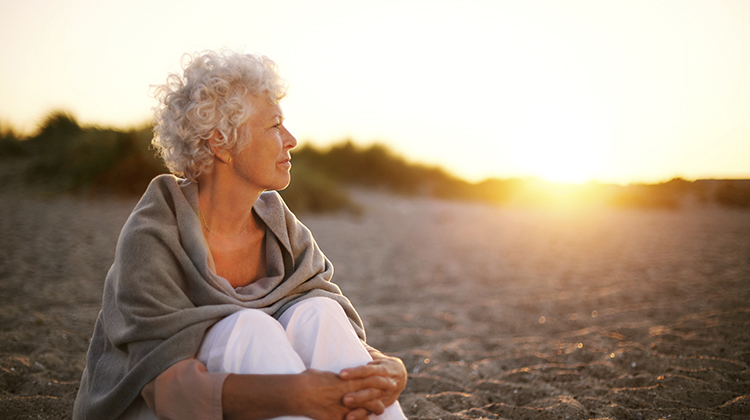Old woman sitting on the beach looking away at copyspace