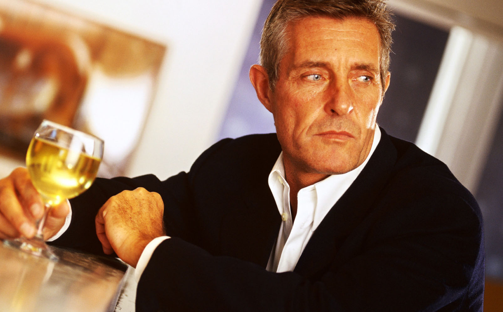 a man sitting by at a bar with a glass of alcohol in his hand